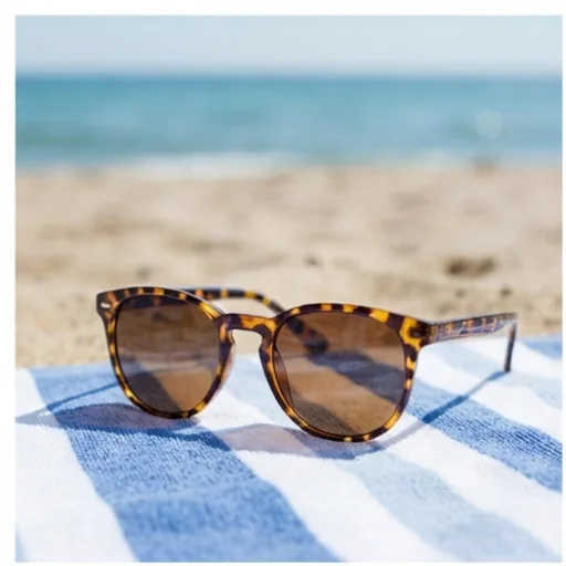 A sunglasses product photo staged on a beach towel by the sea