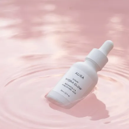 A white skincare serum bottle floating on calm pastel pink water with gentle ripples. Minimal product photography, soft diffused light, clean composition, high-end beauty ad.